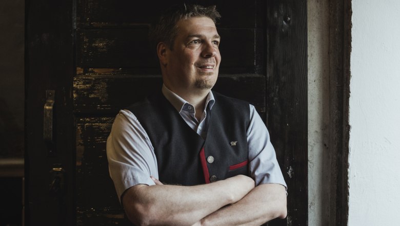 A bérbeadó Dietmar Schöner, © Niederösterreich Werbung/David Schreiber Egy hagyományos öltözetű férfi áll összefont karokkal egy sötét faajtó előtt.