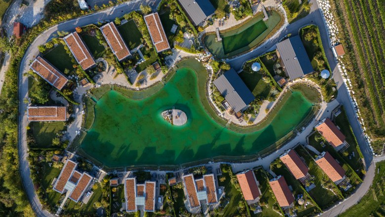 Kittenberger Chalets a Gartensee-nél, © Niederösterreich Werbung / Maximilian Pawlikowsky Légi felvétel a zöld tó körüli faházakról, középen egy mólóval.