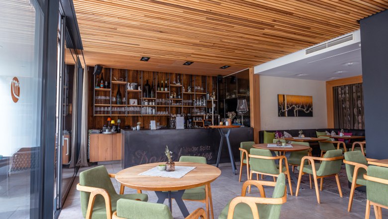 Boutique hotel WeinSpitz, © Niederösterreich Werbung / Maximilian Pawlikowsky A borozó belső nézete, fa elemekkel, zöld székekkel és egy bárral a háttérben.