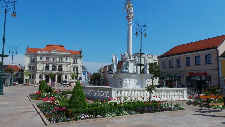 td-hauptplatz-mit-bezirksberichtzehetmayer, © TD-Hauptplatz-mit-Bezirksgericht-c-Zehetmayer Hauptplatz mit barocker Säule und Blumenbeeten, im Hintergrund ein historisches Gebäude.