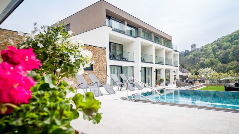 Dunafa © photography pfeffel, © © photography pfeffel Modern épület medencével és napozóágyakkal, zöld vidékkel és egy kastéllyal a háttérben.