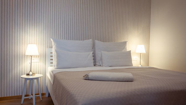 Hausgnost Apartmanok, © Niederösterreich Werbung / Maximilian Pawlikowsky Modern hálószoba franciaággyal, éjjeliszekrényekkel és lámpákkal.