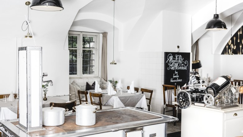 A világos belső tér hangulatos légkört teremt, © Niederösterreich Werbung/David Schreiber Világos éttermi belső tér fehér falakkal, fabútorokkal és egy régi tűzhelyen.