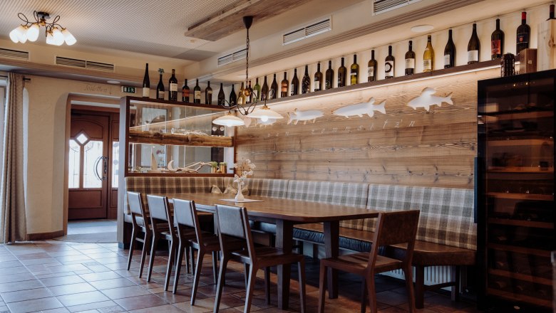 Itt otthon érzed magad, © Niederösterreich Werbung/thecreatingclick.com Hangulatos étkező, fa asztallal, székekkel és paddal, a falon borosüvegekkel és halmotívumokkal díszítve.