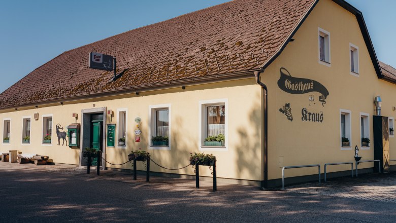 Fogadó természetes kerttel, © Niederösterreich Werbung/Daniela Führer Sárga vendéglő, barna tetővel és zöld ajtóval, felirattal: "Gasthaus Kraus".