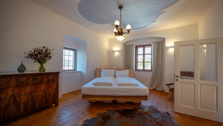 Oberstockstall Estate, © Niederösterreich Werbung / Maximilian Pawlikowsky Hangulatos hálószoba fapadlóval, franciaággyal, antik komóddal és virágcsokorral. Mennyezeti lámpa és függönyös ablak.