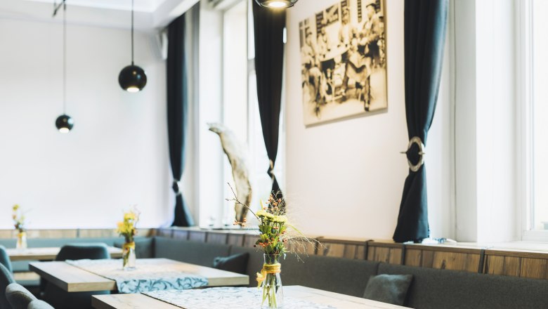 Berndorf szívében, © Niederösterreich Werbung/David Schreiber Egy elegáns kávézó belső nézete, fa asztalokkal, virágvázákkal és fekete függönyökkel.