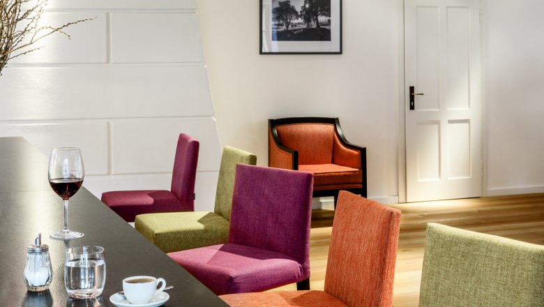 Hotel zum Glockenturm, © croce&wir Belső nézet egy modern szálloda társalgójából, színes székekkel, egy asztallal és italokkal, valamint egy képpel a falon.