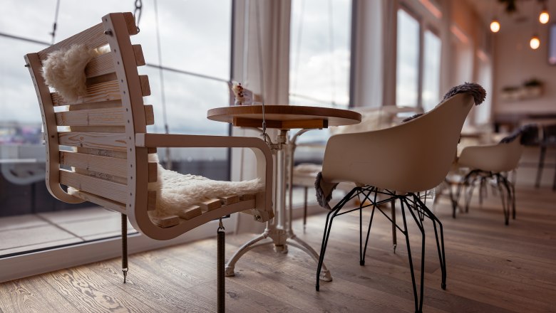 Az Alfréd, © Niederösterreich Werbung / Maximilian Pawlikowsky Egy kávézó belső nézete modern székekkel és fa asztallal, a háttérben nagy ablakok.