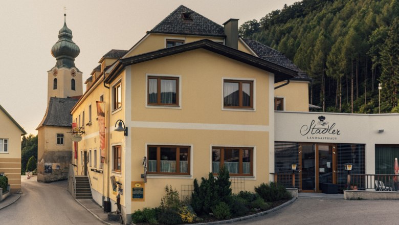 Fogadó Reinsbergben, © Niederösterreich Werbung/Julius Hirtzberger Sárga épület a "Stadler Landgasthaus" felirattal és a háttérben egy templom.