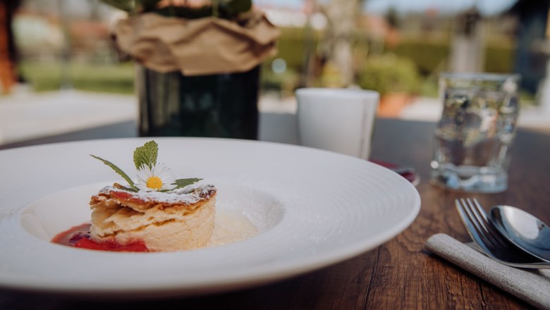 De nem csak halakról van szó. Bizonyíték: Tejkrémes rétes, © Niederösterreich Werbung/thecreatingclick.com Egy tányér tejfölös rétes, százszorszépekkel díszítve, egy kinti faasztalon.