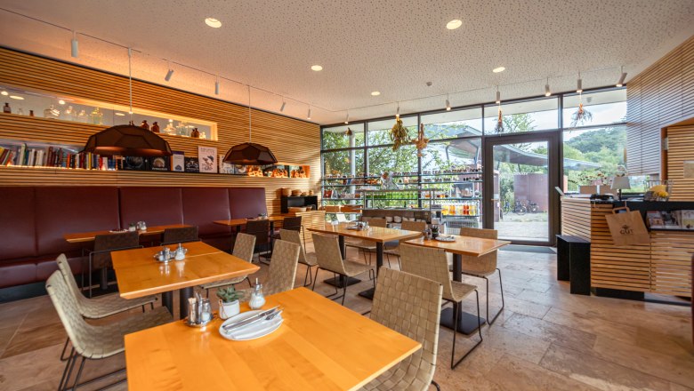 Naturhotel Gut Guntrams Gartenlofts kertészlakások, © Niederösterreich Werbung / Maximilian Pawlikowsky Egy modern étterem belső nézete, faasztalokkal és nagy ablakokkal.