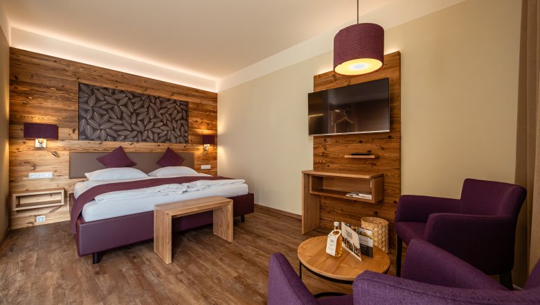 Ágy a Wies'nben, © Niederösterreich Werbung / Maximilian Pawlikowsky Hangulatos szállodai szoba fából készült falakkal, franciaággyal, TV-vel és lila fotelekkel.