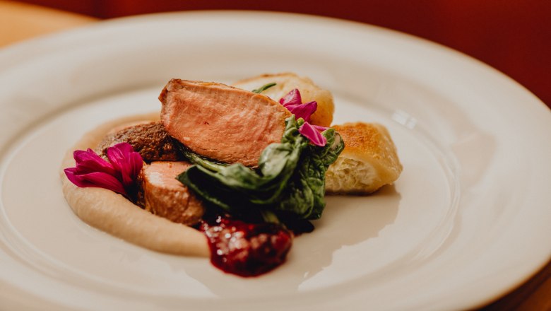 Rózsaszín sült kacsa krémtortával és gesztenyepürével, © Niederösterreich Werbung/Klaus Engelmayer Egy tányér rózsaszínű sült kacsa, tejszínes lepény, gesztenyepüré és zöld levelek, ehető virágokkal díszítve.