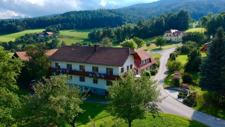 ...körülvéve a természettel., © Familie Rosinger Vidéki táj egy nagy házzal, fákkal és rétekkel körülvéve, felhős ég alatt.