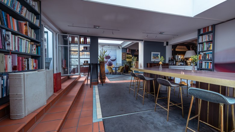 Relais & Chateaux MÖRWALD Hotel am Wagram, © Niederösterreich Werbung / Maximilian Pawlikowsky Egy modern szállodai szoba belső nézete könyvespolcokkal, magas asztalokkal és bárszékekkel.