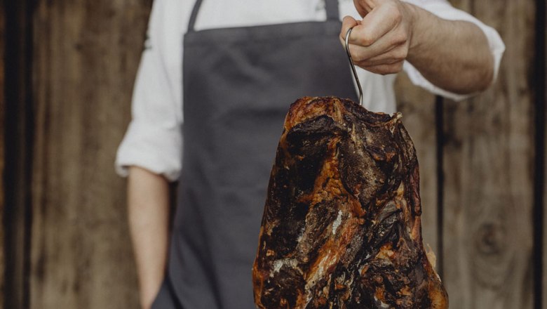 házilag füstölt Emmerberger füstölt sonka, © Niederösterreich Werbung/Sophie Menegaldo Füstölt sonkát tartó személy egy horgon.