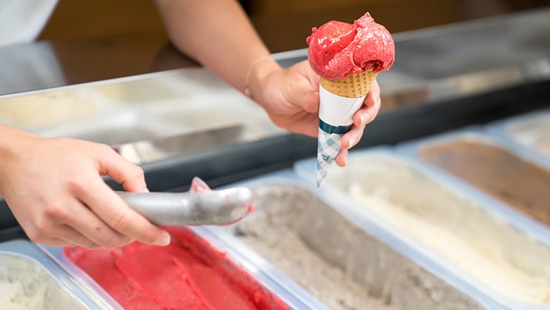 One hand holds an ice cream cone with a scoop of fruit ice cream, the other holds an ice cream scoop., © Blochberger Eisproduktion GmbH One hand holds an ice cream cone with a scoop of fruit ice cream, the other holds an ice cream scoop., © Blochberger Eisproduktion GmbH