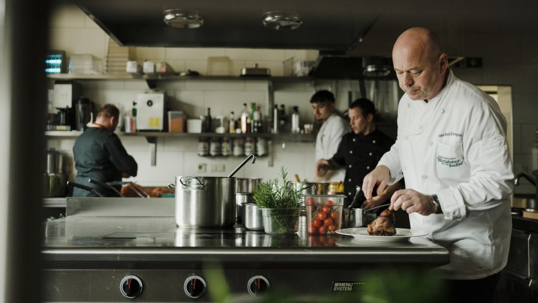 Manfred Hausgnost a konyhában, © Niederösterreich Werbung/Michael Reidinger A szakácsok egy profi konyhában dolgoznak, az egyikük húst vág.