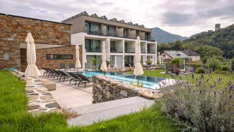 Boutique hotel WeinSpitz, © Niederösterreich Werbung / Maximilian Pawlikowsky Egy modern butikhotel külső nézete medencével és napozóágyakkal, zöld vidék és dombok között.