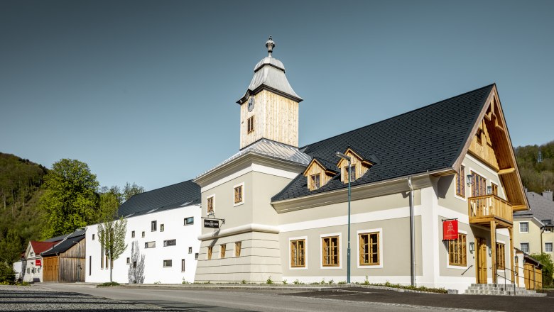 Hotel zum Glockenturm, © croce&wir Modern épület, harangtoronnyal és faburkolattal, fákkal és tiszta égboltal körülvéve.