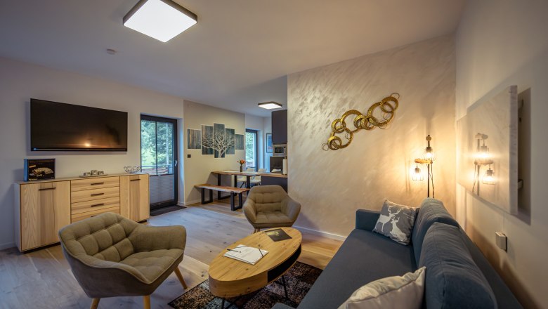 Modern nappali kanapéval, fotelekkel, TV-vel és étkezőasztallal.