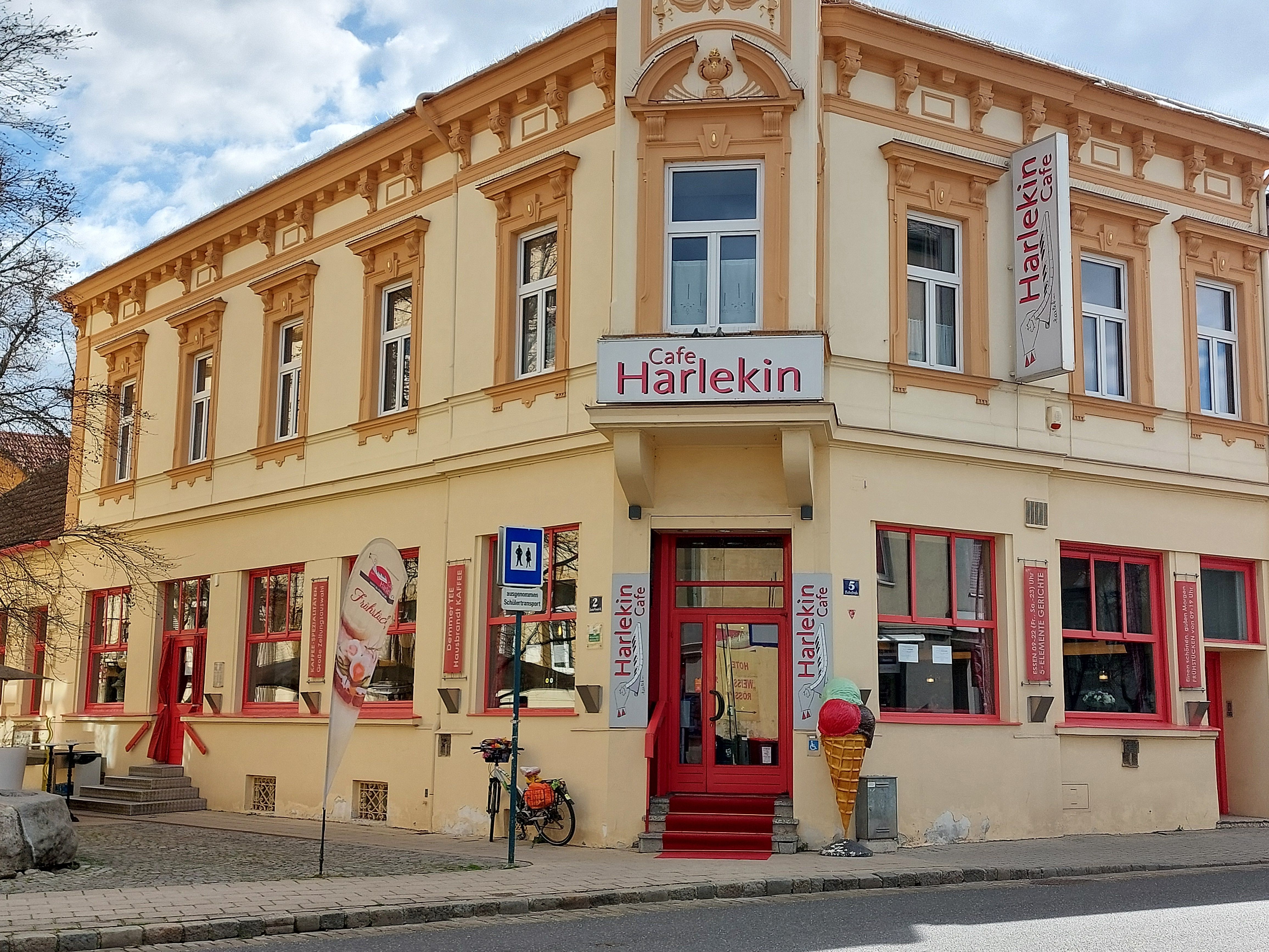 A Cafe Restaurant Harlekin külső nézete sárga homlokzattal és piros ablakokkal.