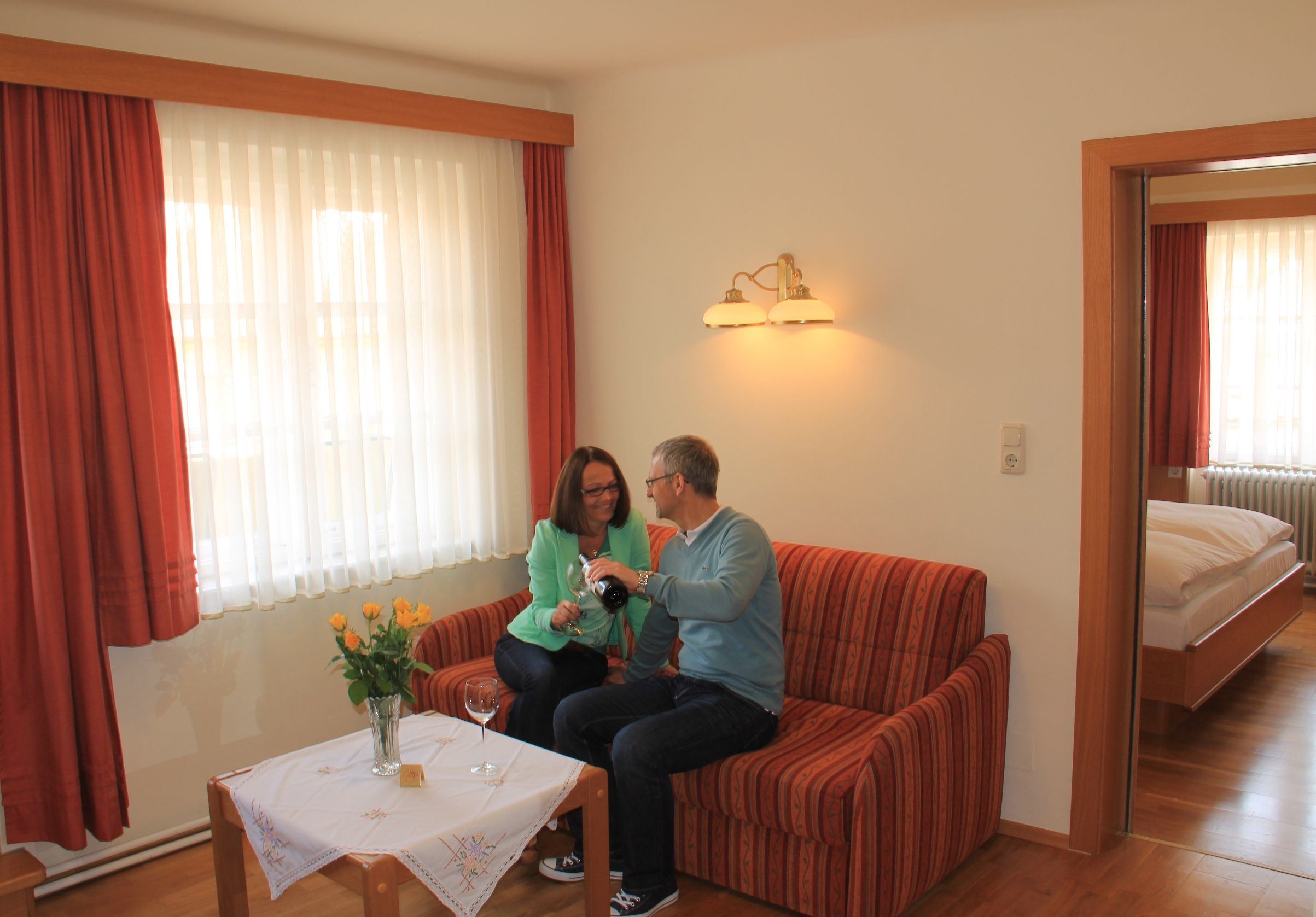 Egy pár ül egy kanapén egy hangulatos lakásban, és bort tölt.