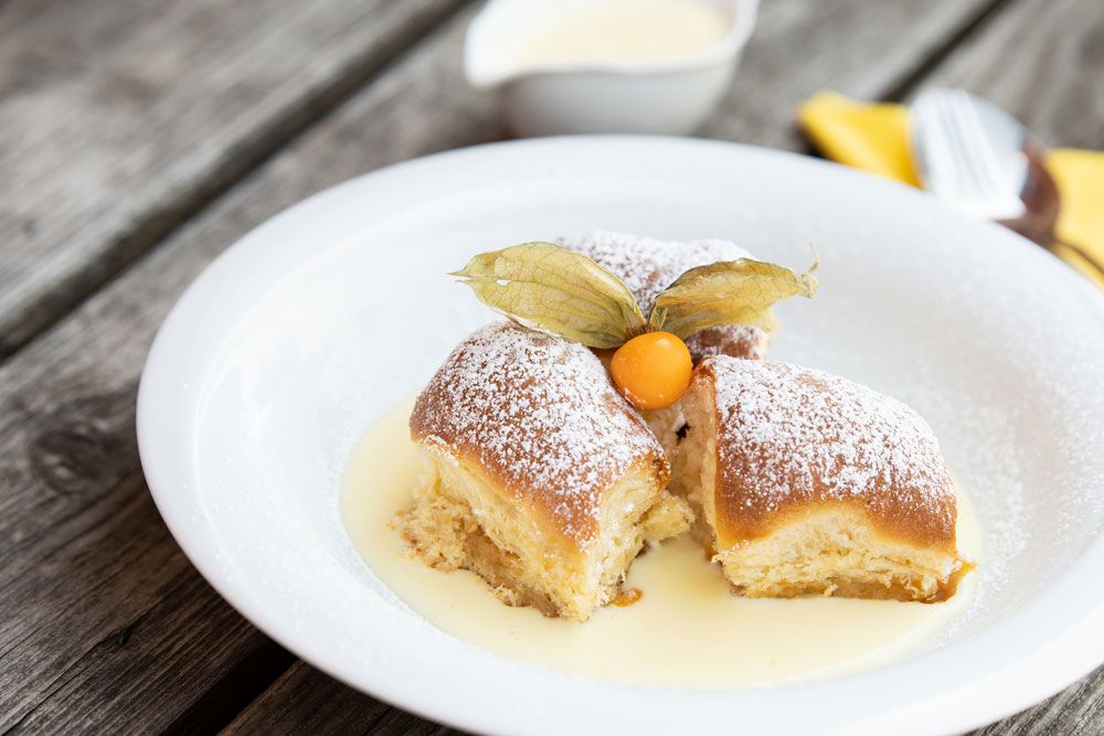 Három Buchteln porcukorral és physalis vaníliamártással fehér tányéron.