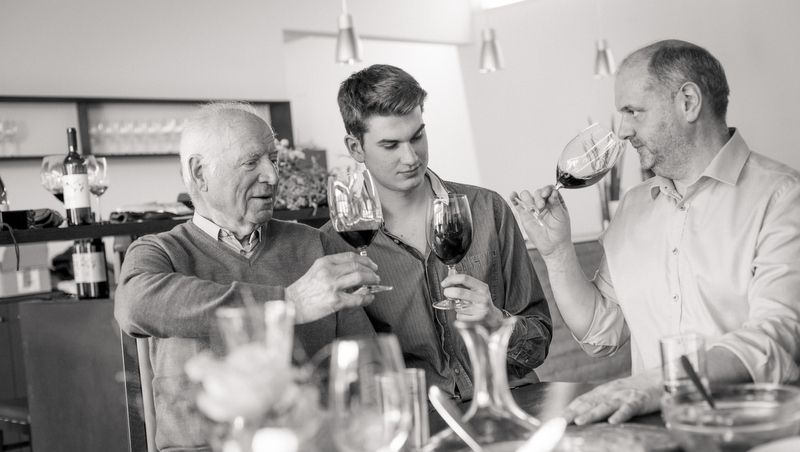 Három férfi koccint egy asztalnál borospoharakkal.