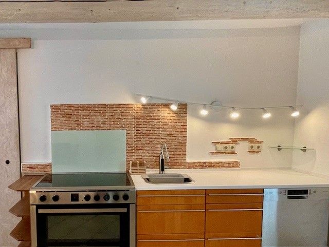 Modern konyha, tűzhely, mosogató és mosogatógép a mozaikcsempézett fal előtt.