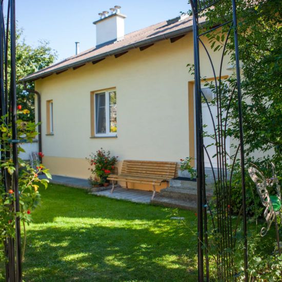Sárga ház, előtérben kerti paddal és virágokkal.