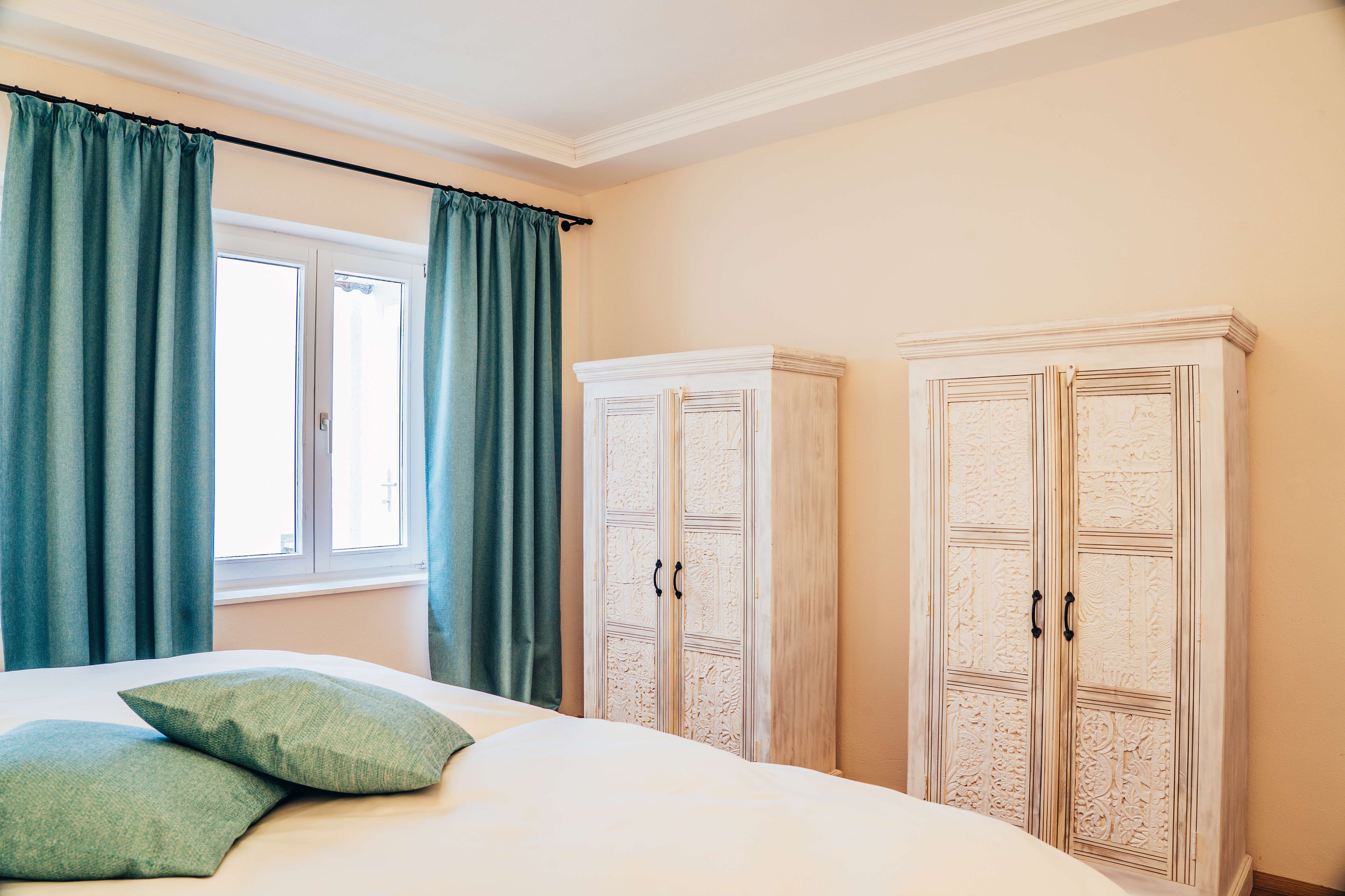 Hálószoba két fehér szekrénnyel, türkiz színű függönyökkel és párnákkal.