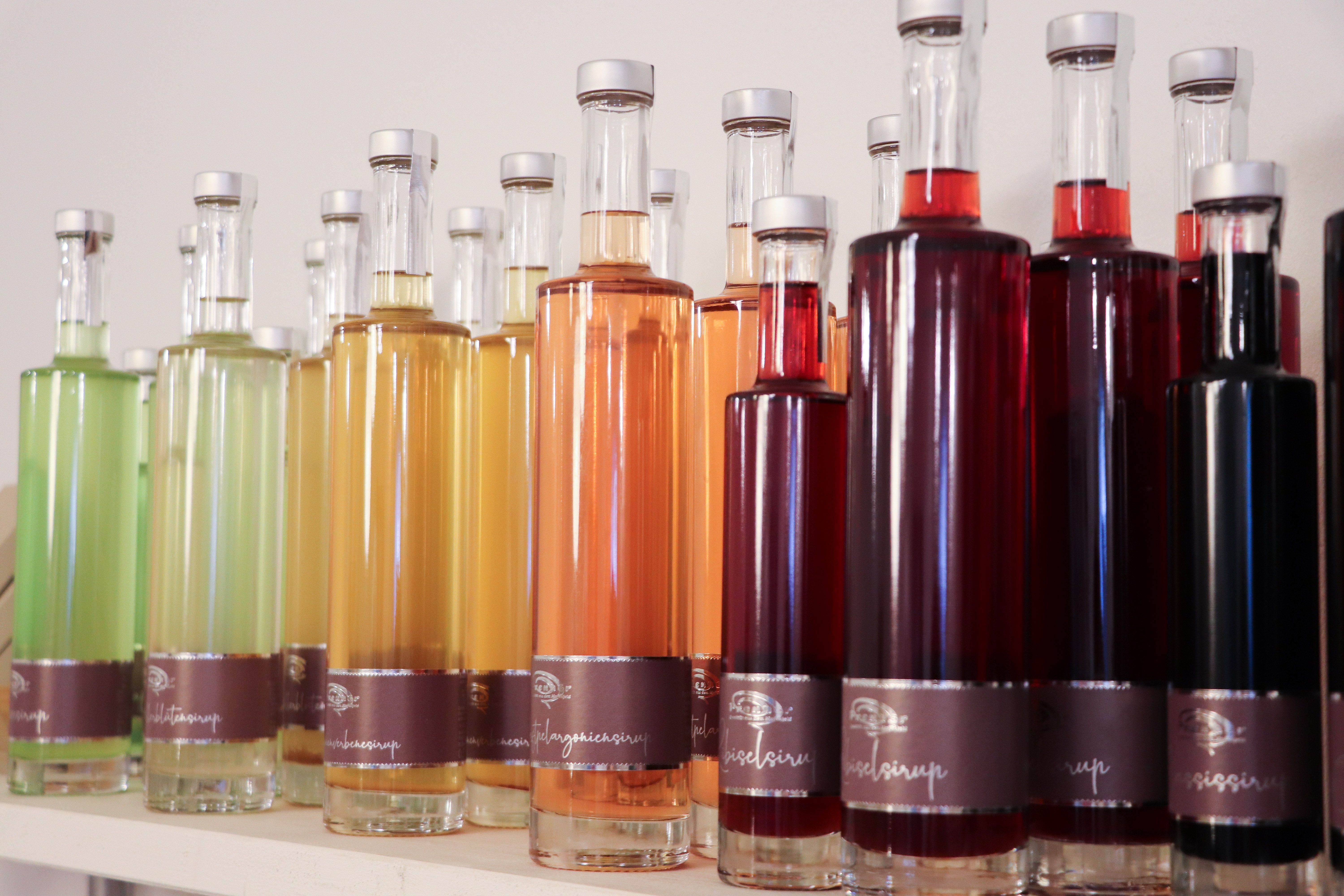 Különböző színes szirupos üvegek sorban egy polcon.