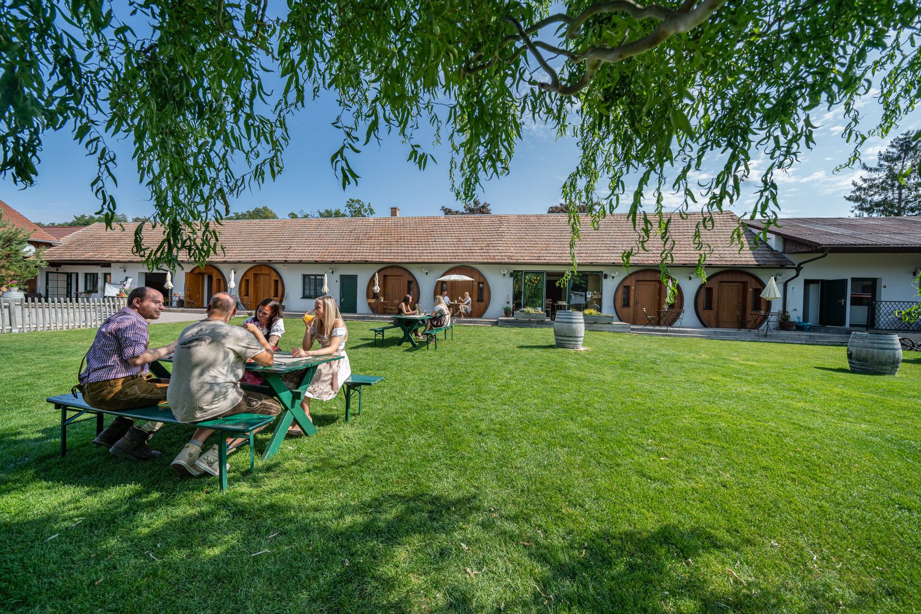 Az emberek egy asztalnál ülnek a gyepen, egy kerek ajtókkal ellátott épület előtt.