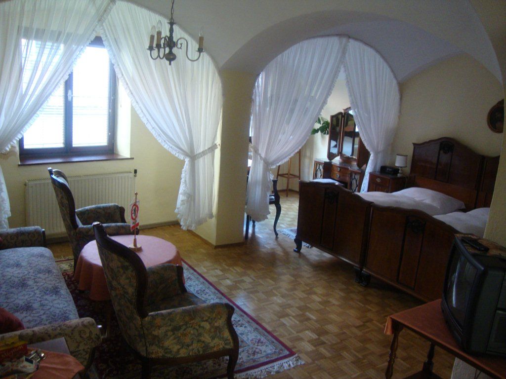Hangulatos vendégszoba antik bútorokkal, franciaággyal, fotelekkel és kis TV-vel. A hálószobát függönyök választják el.