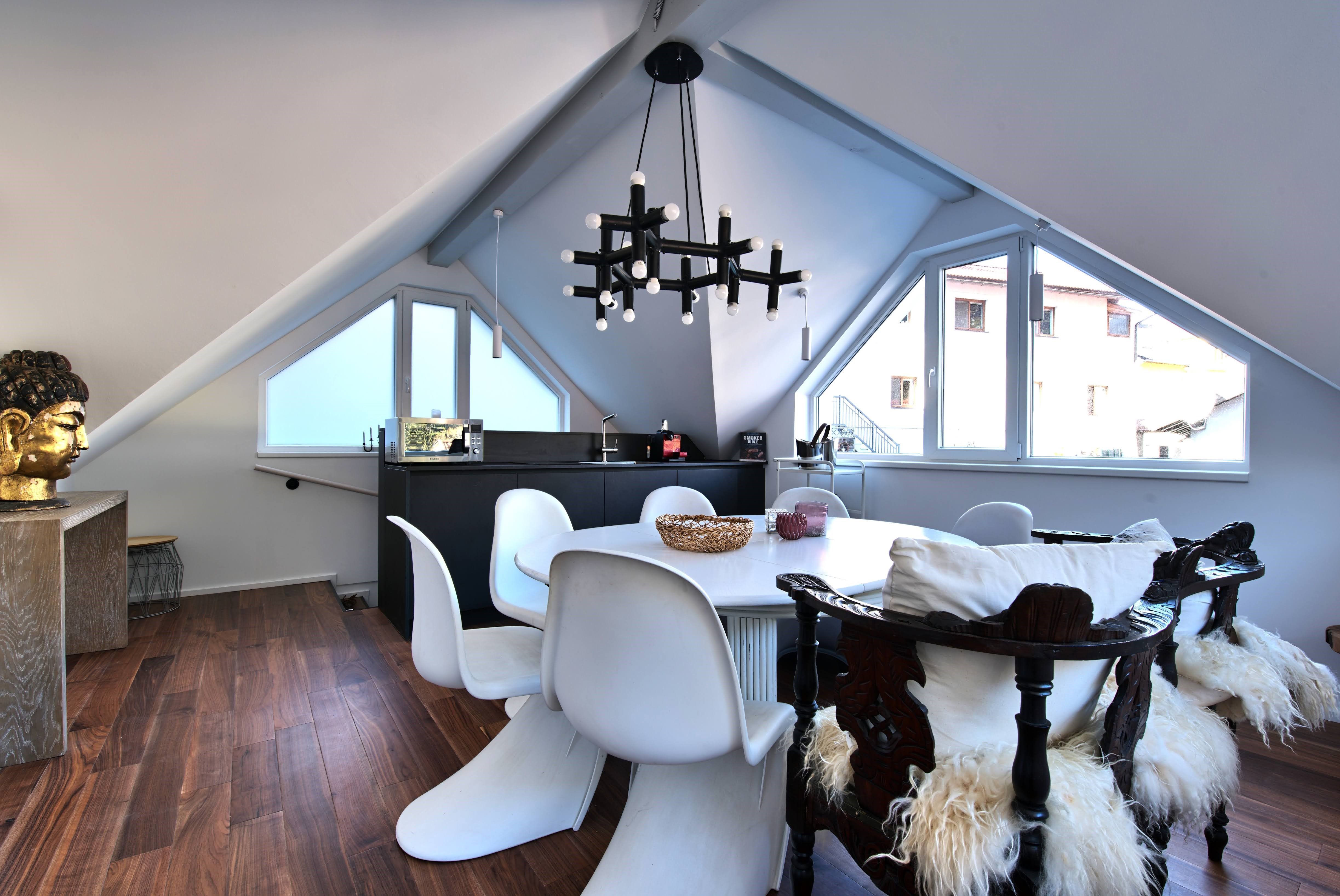 Modern étkező a tetőtérben, fehér székekkel, fapadlóval és nagy ablakkal.