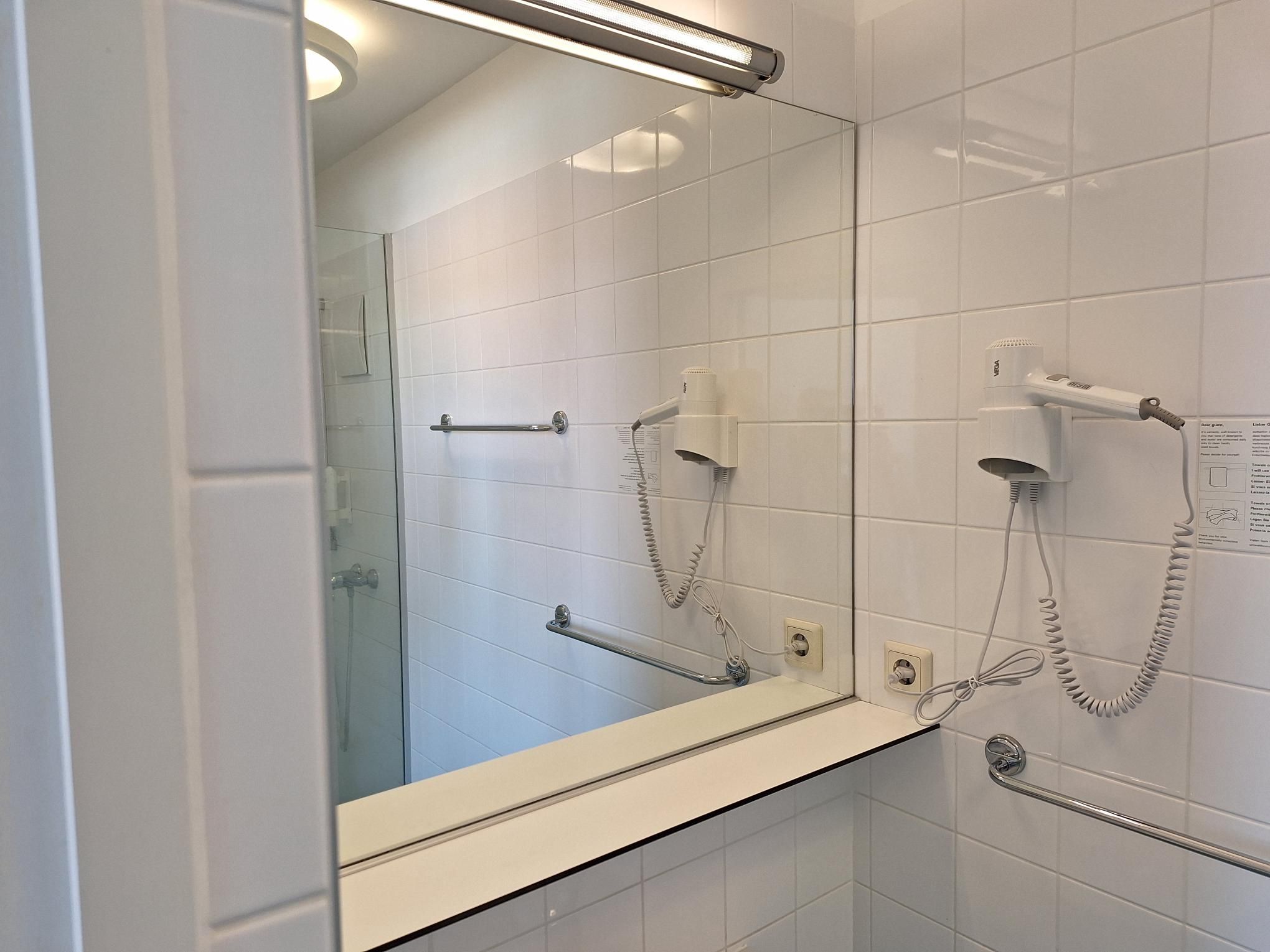 Modern fürdőszoba tükörrel, hajszárítóval és törölközőtartóval.