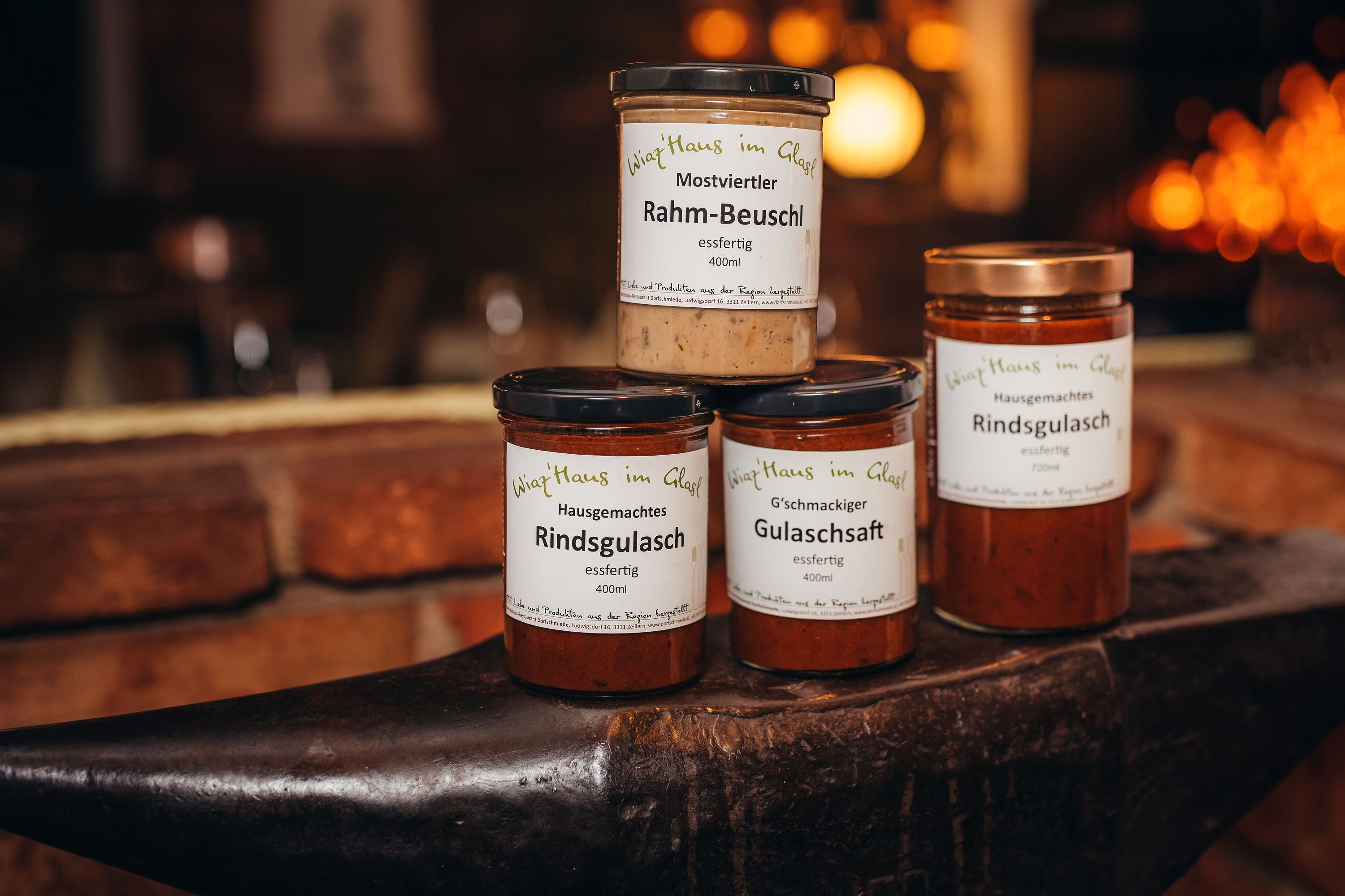 Három üveg készétel egy üllőn, "Wirtshaus im Glas" felirattal.