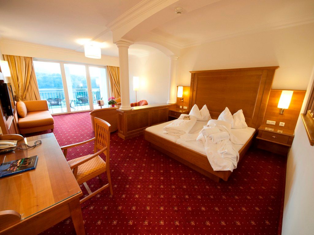 Hotelszoba franciaággyal, íróasztallal és kilátással rendelkező erkéllyel.