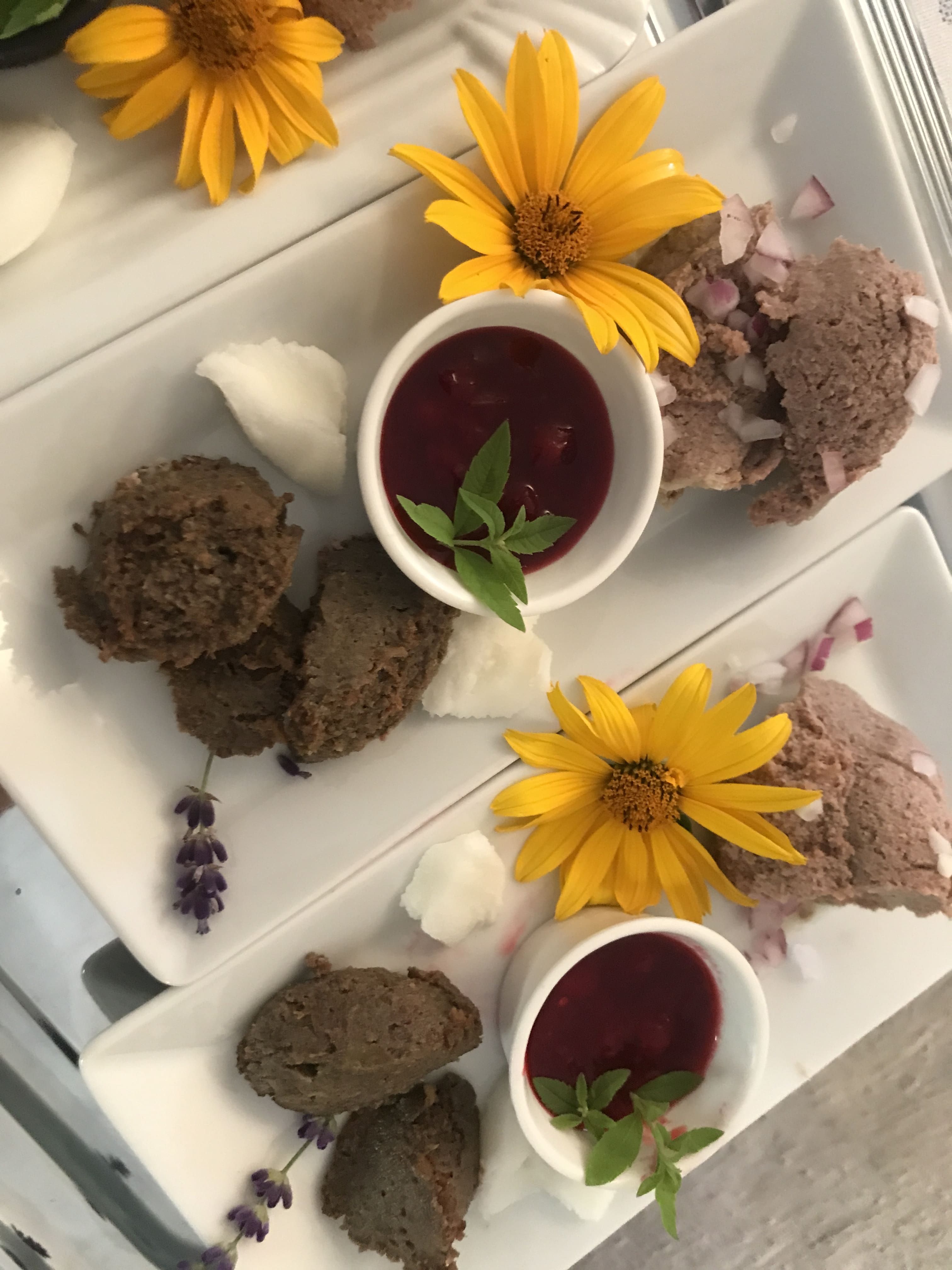 Tányérok terítékkel, sárga virágokkal és piros szószokkal kis tálkákban.