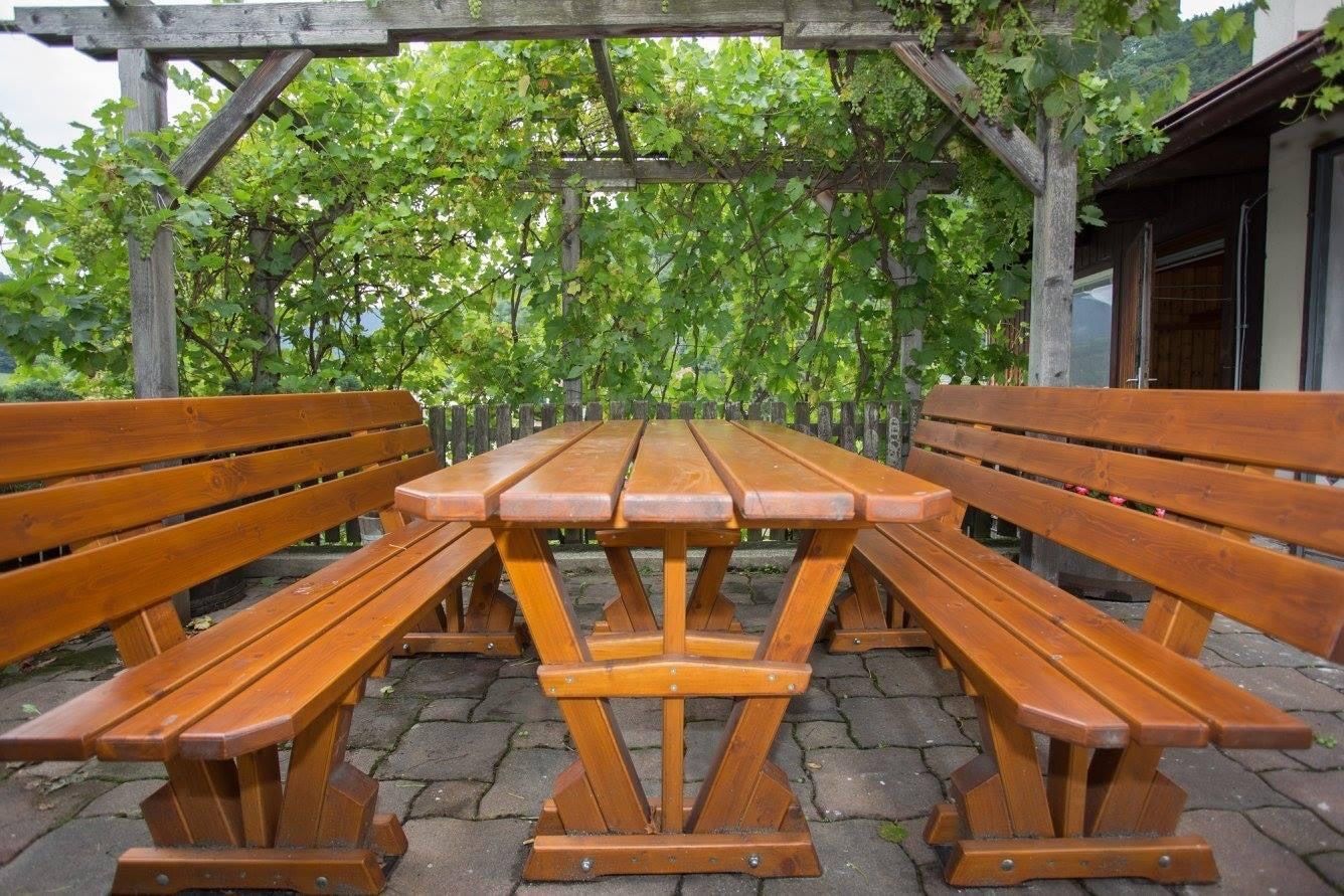 Fa asztal és padok kint egy szőlővel borított pergola alatt.