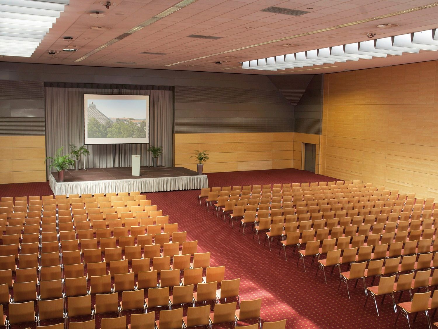 Nagy konferenciaterem színpaddal és széksorokkal.