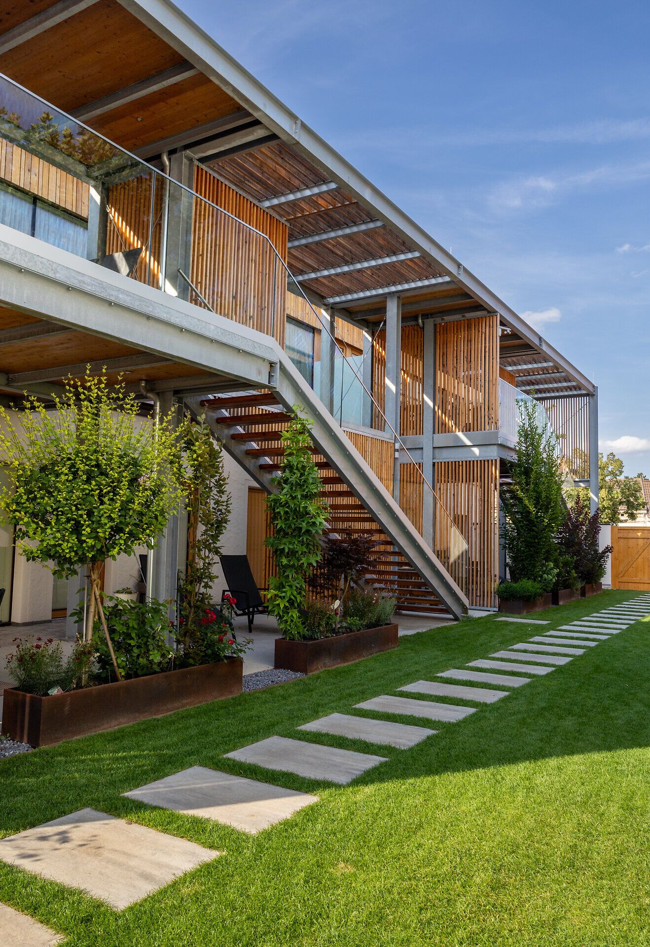 Modern épület fehér homlokzattal és fa elemekkel, fakerítéssel körülvett fal, fa kapuval.