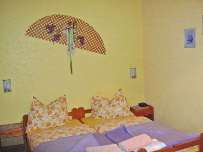 Hangulatos hálószoba sárga falakkal, franciaággyal, mintás párnákkal és dekoratív fali ventilátorral.
