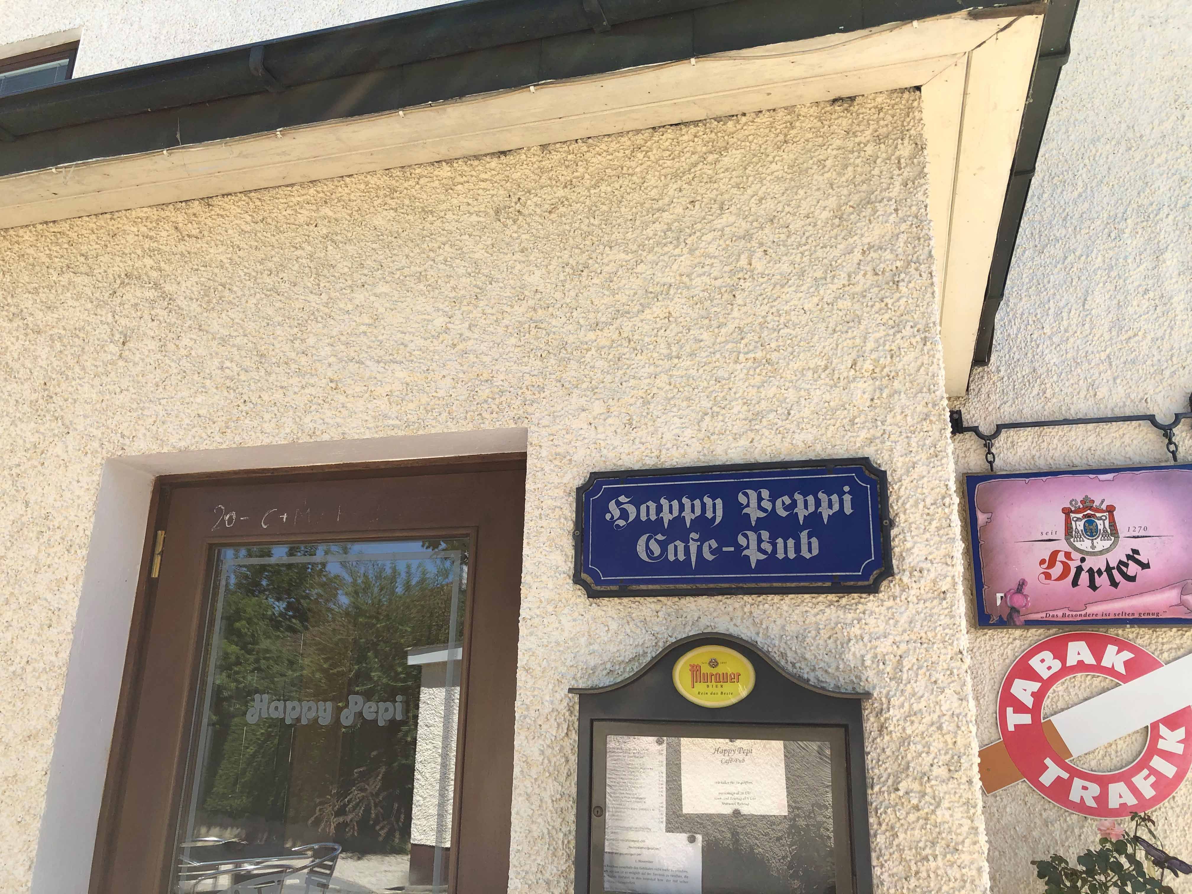 A Happy Pepi kávézó-pub bejárata a falon lévő táblákkal és étlappal.