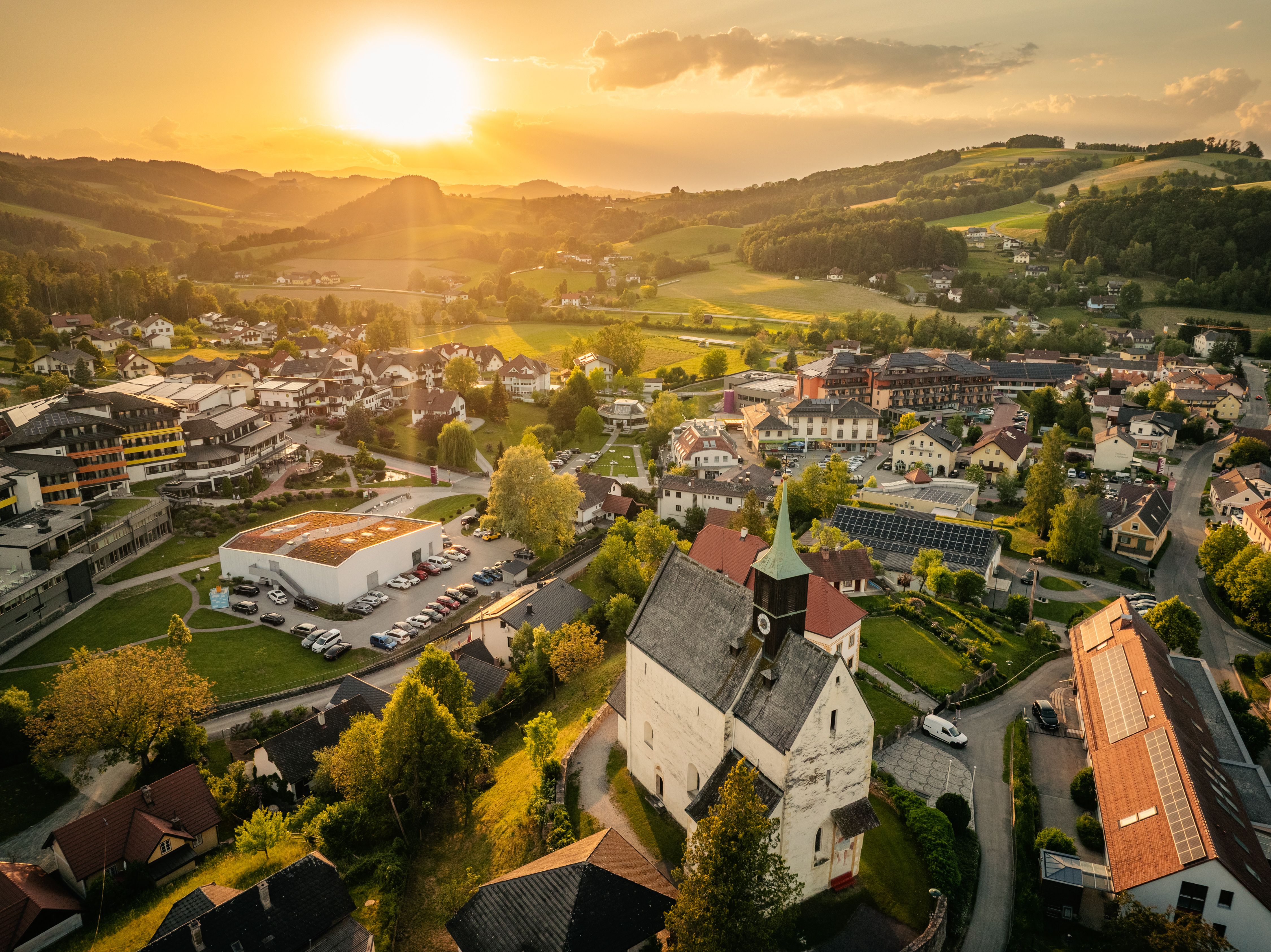 Légi felvétel Bad Schönau városáról naplemente idején, előtérben a Wehrkirche templommal, háttérben a dombokkal.