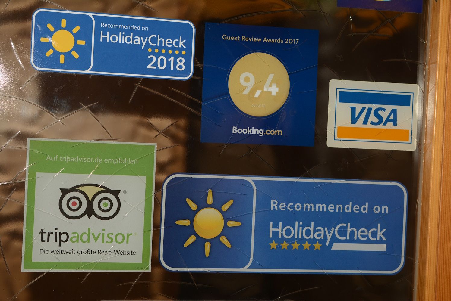 A HolidayCheck, a Booking.com, a TripAdvisor és a Visa matricái egy üvegfelületen.