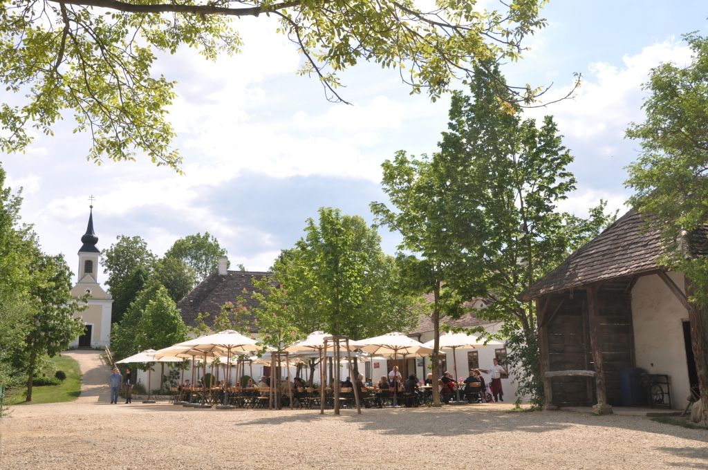 Egy falusi vendéglő a múzeumfaluban, a háttérben napernyőkkel és templommal.