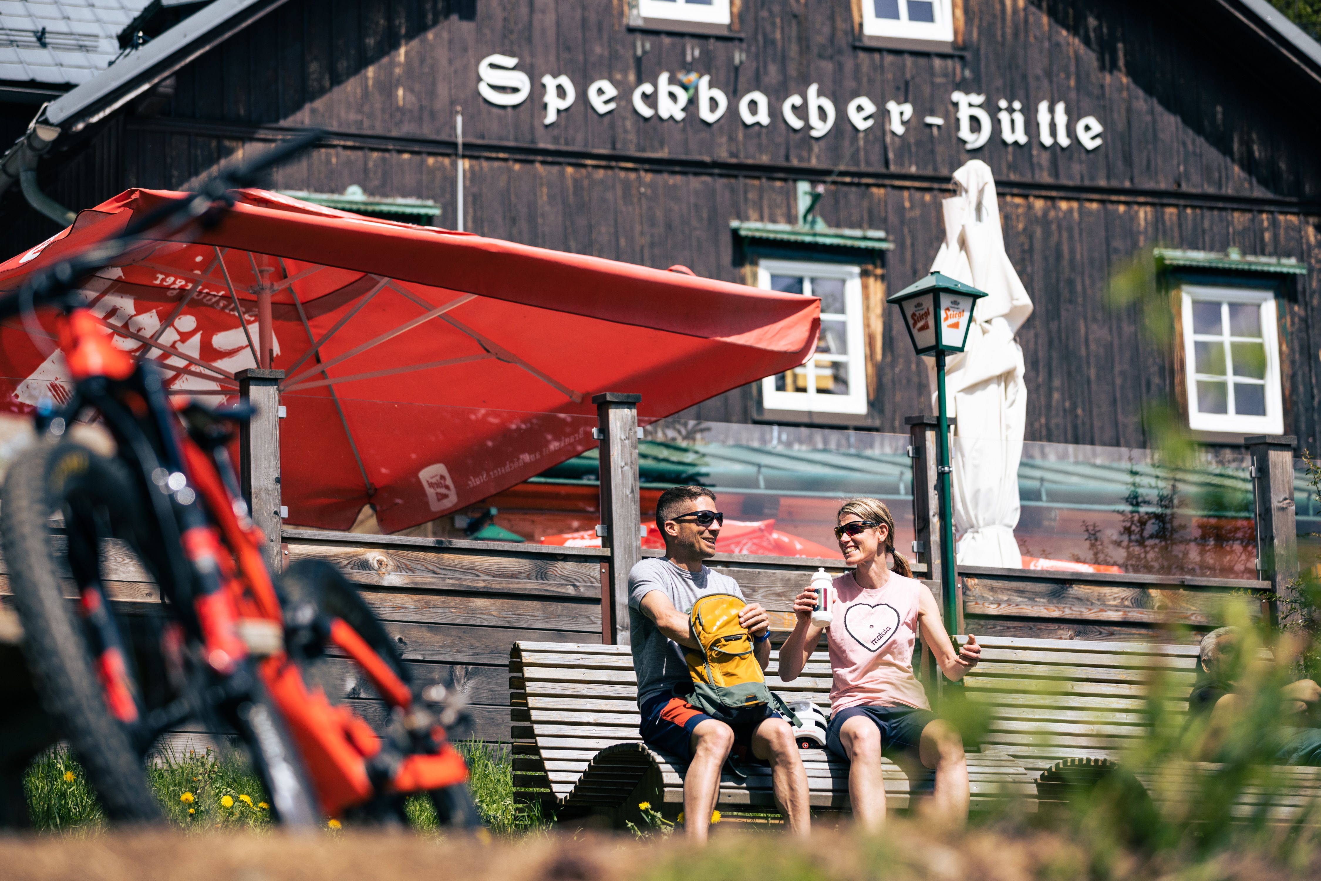 Két ember ül egy padon a Turistaház előtt, előtérben egy mountain bike.